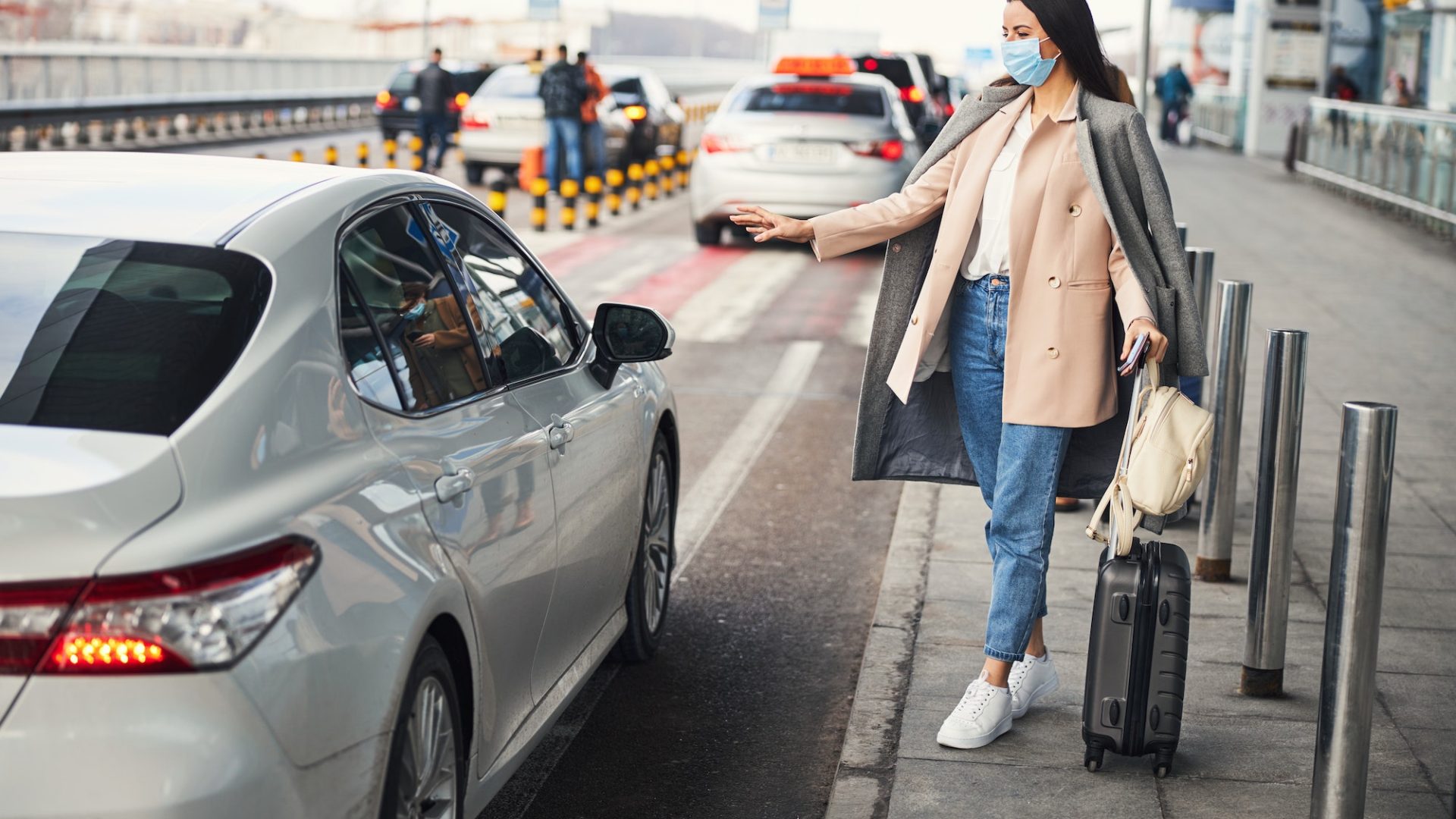 Stylish woman in medical mask taking cab at airport